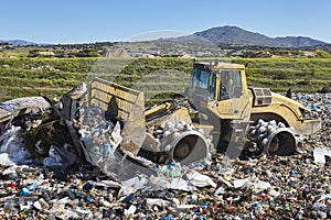 Heavy machinery shredding garbage in an open air landfill. Pollution