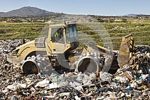 Heavy machinery shredding garbage in an open air landfill. Pollution