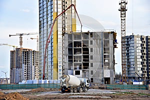 Heavy mixer concrete truck for to be loaded concrete at a construction site. Tower crane lifting a concrete bucket for pouring