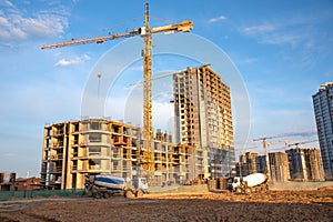 Heavy mixer concrete truck for to be loaded concrete at a construction site. Tower crane lifting a concrete bucket for pouring