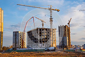 Heavy mixer concrete truck for to be loaded concrete at a construction site. Tower crane lifting a concrete bucket for pouring