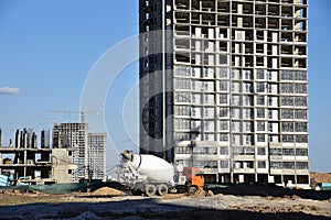 Heavy mixer concrete truck waiting for to be loaded concrete at a construction site. Tower crane lifting a concrete bucket for