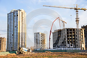 Heavy mixer concrete truck waiting for to be loaded concrete at a construction site. Tower crane lifting a concrete bucket for