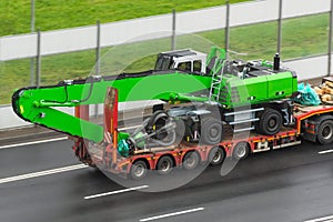 Heavy new green technics long boom claws for gripping scrap metal on transportation truck with rubber wheels long trailer platform