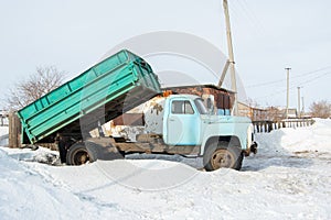 Heavy old blue dump truck with raised body close-up on the background of a snowy road, side view