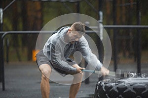 Heavy outdoor training on a rainy day - a man hits a tire with a sledgehammer.