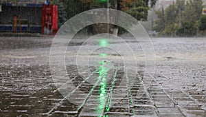 Heavy rain on the sidewalk and asphalt road is illuminated by a green traffic light