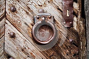 Heavy rusty iron door knocker, ring in front of rectangular iron plate on weathered grained massive old wooden door at the