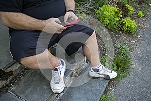 Heavy set, obese Man sitting on a stoop stairs using a cell phone
