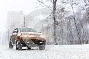 Heavy snowfall and blurred SUV awd car on road. 4wd vehicle on city street at winter. Seasonal roadside assistance concept.