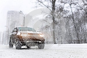 Heavy snowfall and blurred SUV awd car on road. 4wd vehicle on city street at winter. Seasonal roadside assistance concept.