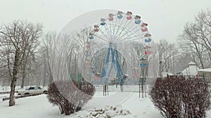 Heavy snowfall in the city, in the Park. View of the snow-covered Ferris wheel in an empty amusement Park on a gloomy