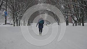 Heavy snowfall in the city. A woman walks along a snowy winter alley.