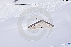 Heavy snowfall covering the mountain house up to the roof. Untouched deep white pure snow drifts in winter Alps