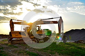Heavy tracked excavator at a construction site on a background of a residential building and construction cranes on a sunny day