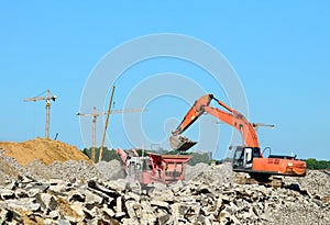 Heavy tracked excavator load stone, old asphalt or concrete waste into a mobile jaw crusher machine.