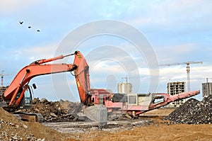 Heavy tracked excavator load stone, old asphalt or concrete waste into a mobile jaw crusher machine.