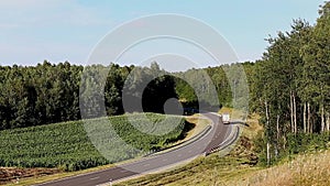 Heavy truck is carrying cargo on the highway in a beautiful area at summer day.