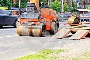 Heavy vibrating road roller is unloaded from a low platform trailer and stands on the roadway