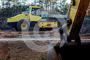 Heavy Vibration roller on sand road as an example of rest between road works. bucket of excavator in foreground