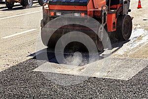 A heavy vibratory road roller compacts asphalt on the road to be repaired