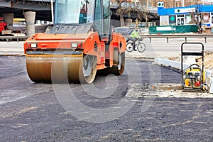 A heavy vibratory roller compacts hot asphalt on the roadway on a clear sunny day