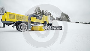 Heavy wheel machinery with big bucket and rotating brush is riding for removing snow and cleaning the roads in the snowy