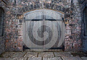 Heavy wooden castle double door with metal bands and studs.  Medieval style set in a stone block wall