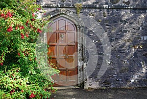 Heavy wooden door set in a dark stone wall with flowers beside