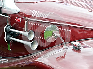 Detail of a red old sports car with mirror, horn and the nickname maude