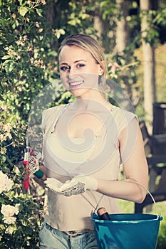 Ñheerful young woman holding horticultural tools in garden