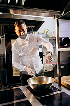 Ð¡hef in the professional kitchen with a frying pan and a fire..Chef`s hands hold iron Pan and preparing food on cooker