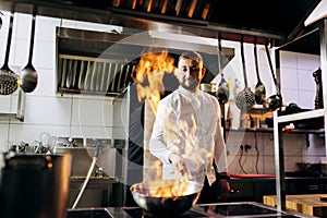 Ð¡hef in the professional kitchen with a frying pan and a fire..Chef`s hands hold iron Pan and preparing food on cooker