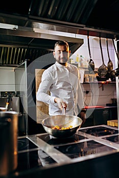 Ð¡hef in the professional kitchen with a frying pan and a fire..Chef`s hands hold iron Pan and preparing food on cooker