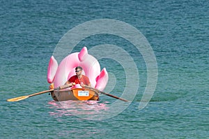 Hel, Poland - 08.01.2021: Beach lifeguard rowing in his orange boat carrying a big pink inflatable flamingo back to the