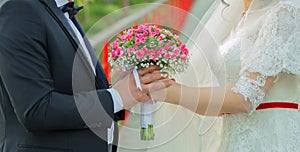 They held the pink flower bouquet in their hands . hands folded behind their back, hold a beautiful little wedding bouquet of rose