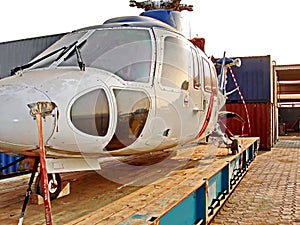 A helicopter without blades is installed on a cargo platform and prepared for loading onto a ro-ro vessel.