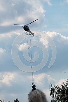 Helicopter with bucket dropping chalk over the forest to improve acid soil.