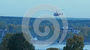 The helicopter collects water in the river to extinguish a fire. The rescue service and firefighters extinguish the fire