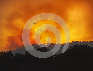 Helicopter fighting forest wildfire at night, dramatic landscape with red sky and heavy smoke