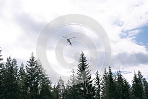 A helicopter flies in the mountains above the forest. Rescuers, air delivery, air taxi helicopter rental, Dolomites mountains,