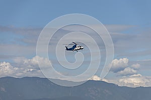 Helicopter flies over the mountains covered with forest, under t