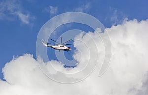 A helicopter flying against a backdrop of a clear blue sky and white clouds