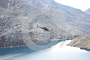 Helicopter flying over a lake, between the mountains of the Langtang National Park