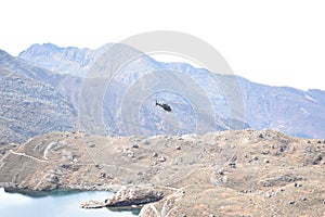 Helicopter flying over a lake, between the mountains of the Langtang National Park