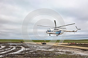 A helicopter lands on a wooden heliport in the tundra.