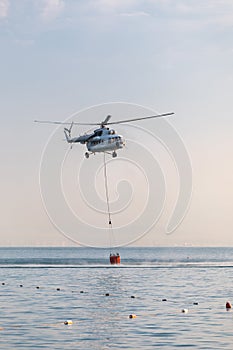 A helicopter with a red basket is lowered over the sea to catch water.