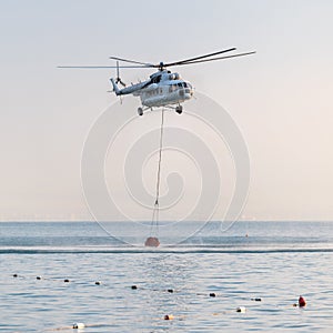 A helicopter with a red basket is lowered over the sea to catch water.