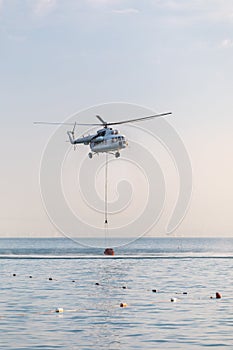 A helicopter with a red basket is lowered over the sea to catch water.
