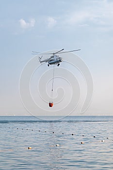 A helicopter with a red basket is lowered over the sea to catch water.